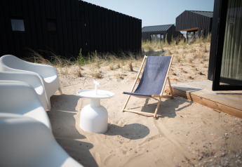 Moderne Stühle und ein Liegestuhl am Sandstrand bei Sea Lodges Zandvoort 3 in den Niederlanden.
