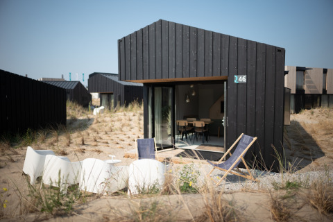 Casa de playa negra y moderna en Sea Lodges Zandvoort 3, Países Bajos, rodeada de dunas y sillas de jardín.