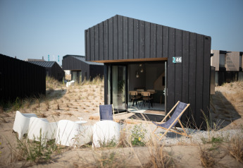 Modernes schwarzes Strandhaus in den Sea Lodges Zandvoort 3, Niederlande, mit Liegestühlen im Sand.