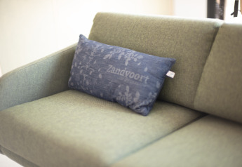 Grünes Sofa mit einem blauen Kissen mit der Aufschrift 'Zandvoort' im Sea Lodges Zandvoort 3 Strandhaus, Niederlande.