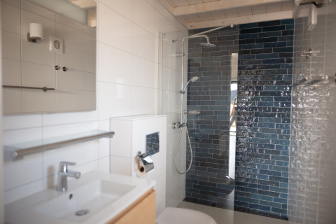 Baño moderno con lavabo blanco, ducha y azulejos azules en Sea Lodges Zandvoort 3 en los Países Bajos.