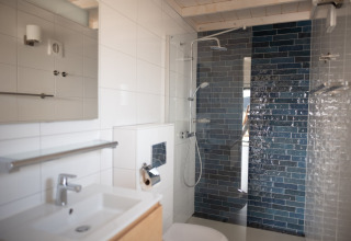 Baño moderno con lavabo blanco, ducha y azulejos azules en Sea Lodges Zandvoort 3 en los Países Bajos.