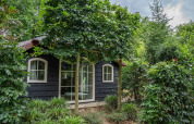 Heivlinder Comfort 4+2p lodge in the Netherlands surrounded by lush garden and tall green trees.