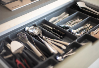 Cajón de cocina abierto con organizador de cubiertos, contiene cucharas, tenedores, cuchillos y utensilios.