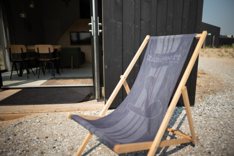 Silla de playa frente a una casa negra con puerta abierta, Sea Lodges Zandvoort 3, Países Bajos.