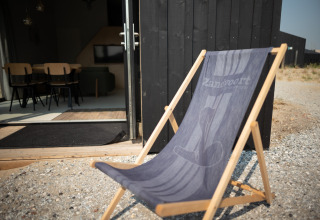 Silla de playa frente a una casa negra con puerta abierta, Sea Lodges Zandvoort 3, Países Bajos.