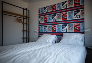 Dormitorio moderno en Sea Lodges Zandvoort 9 con cama doble, pared de carteles coloridos y armario abierto.