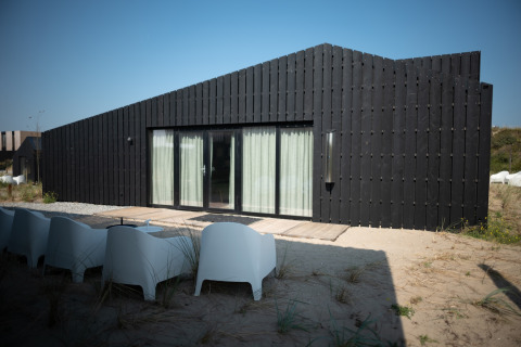 Casa de playa negra moderna Sea Lodges Zandvoort 9 con terraza y sillas blancas sobre la arena y cielo azul.