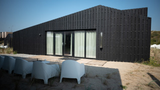 Casa de playa negra moderna Sea Lodges Zandvoort 9 con terraza y sillas blancas sobre la arena y cielo azul.