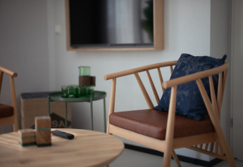 Modernes Wohnzimmer mit Holzstuhl, blauem Kissen, Glastisch und TV in Sea Lodges Zandvoort 9, Niederlande.