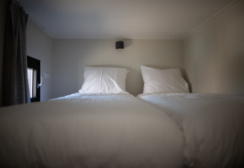 Zwei Einzelbetten mit weißer Bettwäsche in einem kompakten Schlafzimmer der Sea Lodges Zandvoort 9, Niederlande.