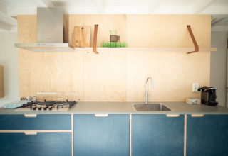 Cocina moderna con armarios azules, pared de madera, estufa de gas y fregadero en Sea Lodges Zandvoort 9.