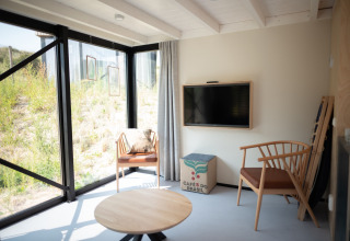 Sala luminosa en Sea Lodges Zandvoort 9 con muebles de madera, ventana grande y vista a las dunas, Países Bajos.
