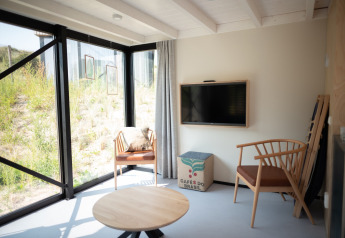 Helles Wohnzimmer in Sea Lodges Zandvoort 9, mit Holzmöbeln, großem Fenster und Dünenblick, Niederlande.