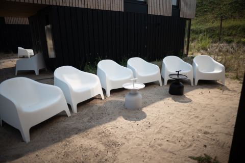 Sillas blancas y mesas exteriores sobre arena en Sea Lodges Zandvoort 9, Países Bajos, junto a una casa moderna negra.