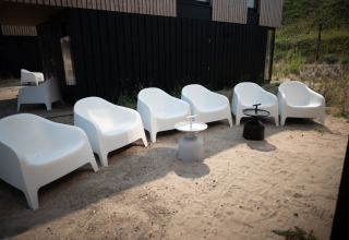 Sillas blancas y mesas exteriores sobre arena en Sea Lodges Zandvoort 9, Países Bajos, junto a una casa moderna negra.