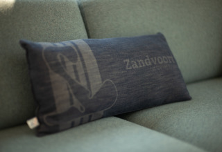 Un cojín oscuro con la palabra 'Zandvoort' se apoya en un sofá verde en la casa Sea Lodges Zandvoort 9.