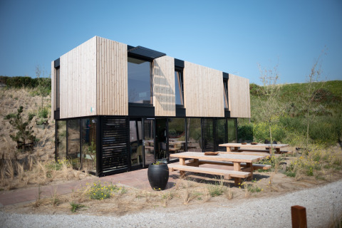 Modern beach house Sea Lodges Zandvoort 11 with wooden exterior, large windows, and outdoor benches.