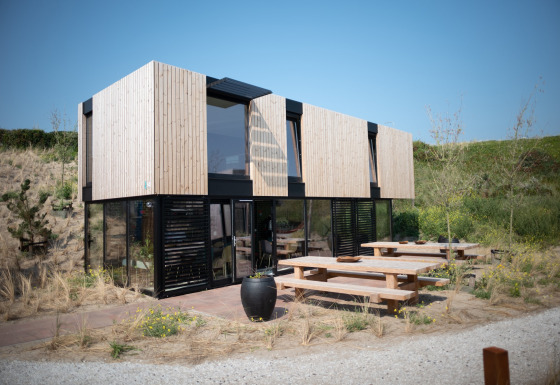 Modern beach house Sea Lodges Zandvoort 11 with wooden exterior, large windows, and outdoor benches.