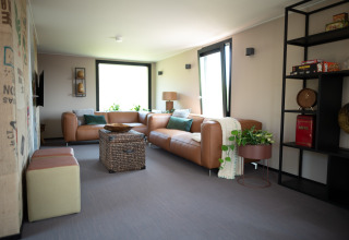 Modern living room at Sea Lodges Zandvoort 11 featuring leather sofas, large windows, and cozy decor.
