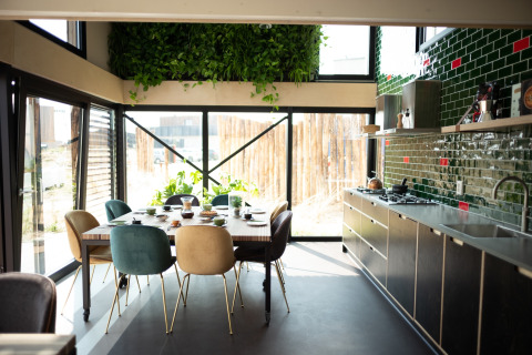 Modern beach house kitchen and dining area with green tiles, plants, and large windows in Zandvoort, Netherlands.