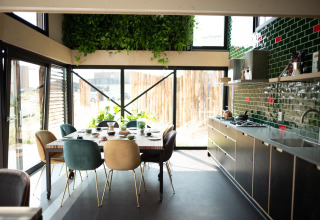 Modern beach house kitchen and dining area with green tiles, plants, and large windows in Zandvoort, Netherlands.