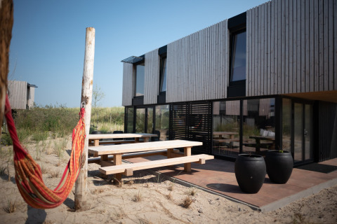 Outdoor terrace at Sea Lodges Zandvoort 11 in the Netherlands, with picnic benches and hammock in sand.