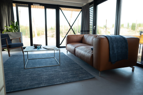 Moderne woonkamer in Sea Lodges Zandvoort 6, Nederland, met lederen zetel, blauw tapijt en grote ramen.