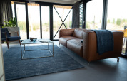 Moderne woonkamer in Sea Lodges Zandvoort 6, Nederland, met lederen zetel, blauw tapijt en grote ramen.