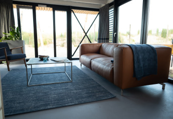 Moderne woonkamer in Sea Lodges Zandvoort 6, Nederland, met lederen zetel, blauw tapijt en grote ramen.