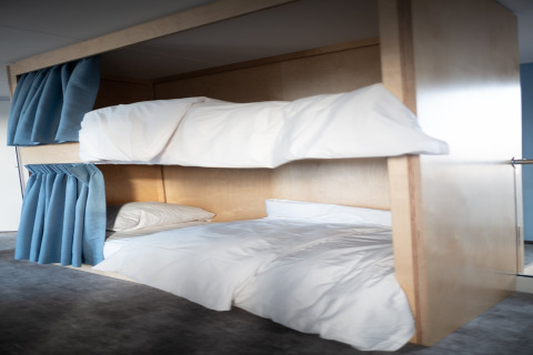 Moderne stapelbedden met witte lakens en blauwe gordijnen bij Sea Lodges Zandvoort 6, strandhuis, Nederland.