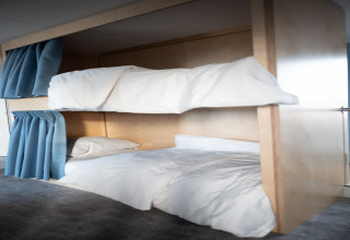 Moderne stapelbedden met witte lakens en blauwe gordijnen bij Sea Lodges Zandvoort 6, strandhuis, Nederland.
