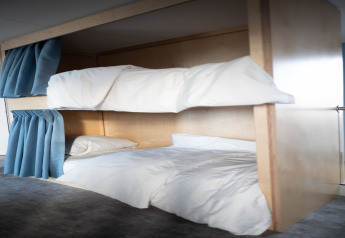Moderne stapelbedden met witte lakens en blauwe gordijnen bij Sea Lodges Zandvoort 6, strandhuis, Nederland.