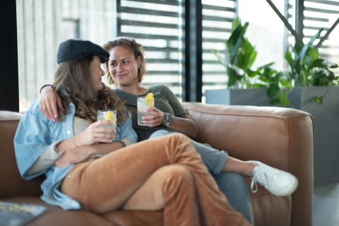 Twee vrouwen relaxen met drankjes op de sofa bij Sea Lodges Zandvoort 6 strandhuis in Nederland.