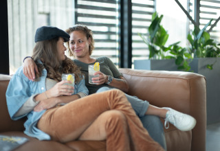 Twee vrouwen relaxen met drankjes op de sofa bij Sea Lodges Zandvoort 6 strandhuis in Nederland.