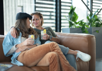 Twee vrouwen relaxen met drankjes op de sofa bij Sea Lodges Zandvoort 6 strandhuis in Nederland.