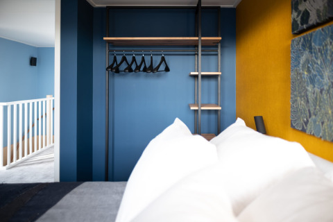 Slaapkamer met een moderne open kast, blauwe muren en gele accentmuur in Sea Lodges Zandvoort 6, Nederland.