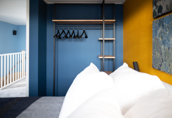Slaapkamer met een moderne open kast, blauwe muren en gele accentmuur in Sea Lodges Zandvoort 6, Nederland.