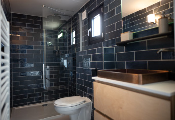 Moderne badkamer met donkerblauwe tegels, glazen douche, toilet en raam in Sea Lodges Zandvoort 6, Nederland.