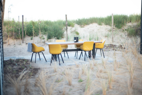 Buitenterras met gele stoelen en een tafel op zand bij Sea Lodges Zandvoort 6 in Nederland, met zicht op duinen.