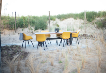 Buitenterras met gele stoelen en een tafel op zand bij Sea Lodges Zandvoort 6 in Nederland, met zicht op duinen.