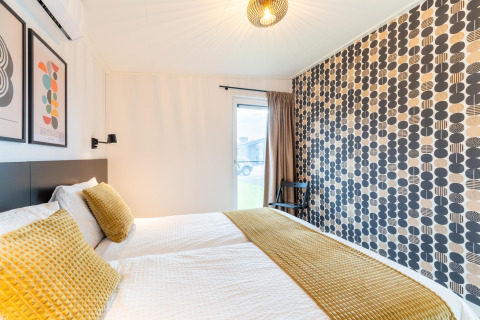 Modern bedroom with patterned feature wall, yellow bedding and pillows at By the Baker lodge in the Netherlands.
