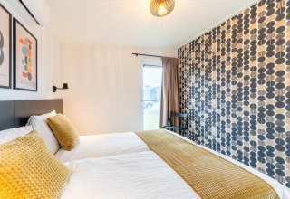 Modernes Schlafzimmer mit gemusterten Wänden und gelber Bettwäsche in der Lodge By the Baker, Niederlande.