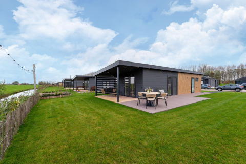 Modern lodge at By the Baker with patio, outdoor dining, large green lawn, and nearby parking area.