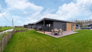 Modern lodge at By the Baker with patio, outdoor dining, large green lawn, and nearby parking area.