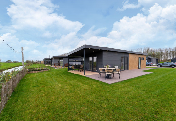 Modern lodge at By the Baker with patio, outdoor dining, large green lawn, and nearby parking area.