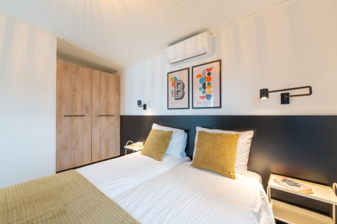 Modern bedroom at 'By the Baker' lodge in the Netherlands with twin beds, wooden wardrobe, and wall art.