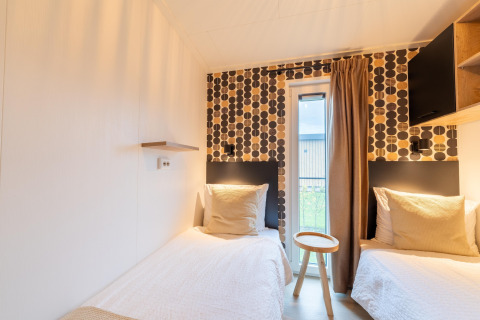 Modernes Lodge-Zimmer mit zwei Einzelbetten, geometrischer Tapete und kleinem Fenster in den Niederlanden.