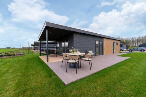 Modern ‘By the Baker’ lodge in the Netherlands with covered terrace, outdoor furniture, and spacious green lawn.