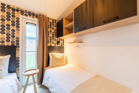 Helles Schlafzimmer mit zwei Einzelbetten, kreativer Tapete und schwarzen Schränken in der Lodge «By the Baker» in den Niederlanden.